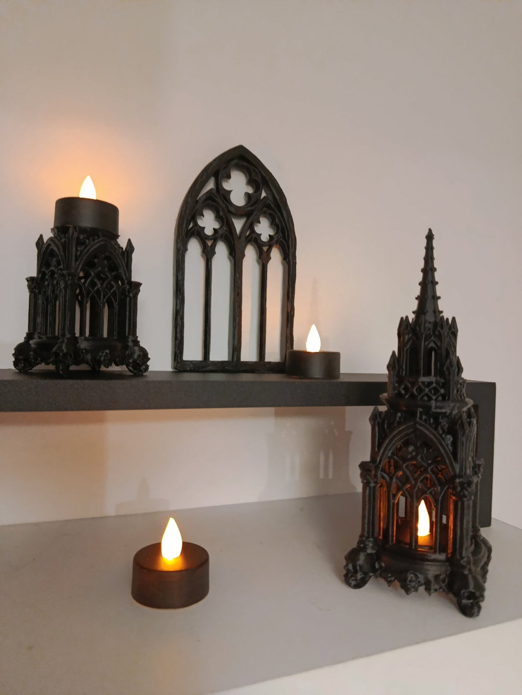 A set of gothic art on a white table with candles illuminating them